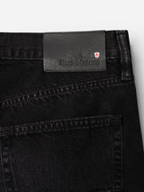 Close-up of the back pocket and waistband of BGmarco Connor Jeans - Black Denim Used, crafted from 100% cotton black denim in a relaxed fit, featuring a black leather label with the Blue de Gênes brand name and a small red and white shield logo.