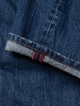 A close-up of dark blue cotton denim BGmarco Sioux Jeans - Used by Blue de Gênes with a cuffed hem, revealing the selvedge edge featuring a red and white stripe detail. The fabric texture and stitching are clearly visible, emphasizing the quality craftsmanship of these jeans.