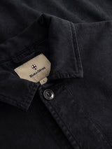 Close-up of the BGbarnaba Iro Overshirt in navy, featuring a black collared design with a single visible button and an inner collar label that reads “Blue de Gênes,” topped with a red and white shield logo. This workwear-inspired overshirt is crafted from a soft lyocell-cotton blend for lasting comfort and durability.