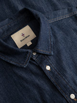 Close-up of the BGgregor Denim Shirt in denim blue by Blue de Gênes, featuring white buttons and visible stitching along the seams. The label inside the collar displays the Blue de Gênes name, size L, and a small shield logo. This shirt is made from cotton.