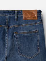 Close-up of the back pocket and waistband of the BGrepi Callum Jeans in mid blue denim by Blue de Gênes, featuring a brown leather patch embossed with the brand name near a small stitched flag detail, crafted from comfort stretch denim for added flexibility.