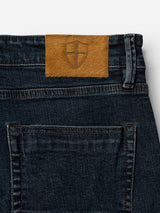 Close-up of the back waistband and pocket of BGvinci Ewan Jeans - Color Denim by Blue de Gênes, featuring a brown leather patch with a shield emblem above the pocket, crafted from comfort stretch denim for enhanced ease of movement.