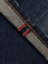 Close-up of the BGvinci Finlay Jeans - Vintage Wash by Blue de Gênes, crafted from dark blue comfort stretch denim with a visible selvedge edge, featuring distinctive red and white stitching details and orange thread along the seam.