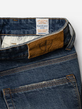Close-up of the BGrepi Presley Jeans - Denim Blue by Blue de Gênes, featuring durable comfort stretch denim, a brown leather patch with a cross symbol on the waistband, a Candiani Denim tag, and two back pockets with prominent orange stitching.