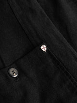 A close-up of the BGduncan Ian Gilet in black by Blue de Gênes showcases a button and a small shield-shaped pin adorned with a red cross on a white background. Crafted from lightweight textured linen, this gilet exudes subtle sophistication and classic style.