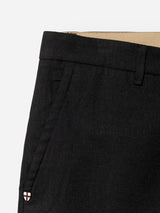 Close-up of the BGpalco Ian Pant - Black by Blue de Gênes, featuring a relaxed fit, slanted front pocket with a beige inner lining, belt loop, and a small patch displaying a white shield with a red cross near the pocket opening.