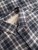 A close-up of the BGenrico Hang Shirt - Navy Check by Blue de Gênes showcases its blue, gray, and white plaid pattern, highlighting the collar, top buttons, and part of an interior tag featuring a small red and blue cross design. Crafted from 100% cotton, this classic check shirt offers lasting comfort and timeless style.