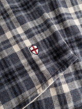A close-up of blue and white plaid fabric from the BGenrico Hang Shirt - Navy Check by Blue de Gênes, featuring a small embroidered shield with a red cross on a white background.