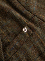 Close-up of the BGleopardi Skotch Blazer in Brown Check by Blue de Gênes, showcasing its brown tweed fabric with thin blue and yellow lines, and featuring a small silver shield-shaped pin with a black cross design attached to the textured check wool.
