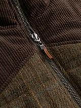Close-up of a metal zipper on the BGalec Skotch Waistcoat - Brown Check by Blue de Gênes, showcasing brown corduroy panels above and green tweed with a checked wool plaid pattern below. A small brown leather tab is attached to the zipper pull.