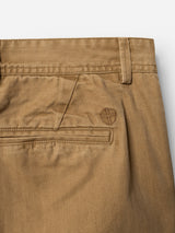 Close-up of the BGmenzo Rory Chino - Khaki by Blue de Gênes, featuring a belt loop, front pocket, back pocket with flap, and a small embroidered shield emblem above the pocket. The fabric displays a subtle herringbone texture reminiscent of classic chino fit washed herringbone trousers.