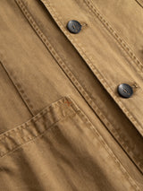 Close-up of the Blue de Gênes BGgabbiano Rory Blazer in Khaki, crafted from tan washed herringbone fabric with black buttons and a front pocket. Featuring an unconstructed design for a relaxed fit, this blazer displays a small area of frayed stitching near the top left corner of the pocket.