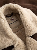 Close-up of the BGseras Shearling Coat in dark brown, featuring a cream, fluffy inner lining. A fabric tag inside the collar displays the Blue de Gênes logo and brand name, highlighting the thoughtful details of this cold-weather coat.