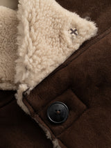 Close-up of the BGseras Shearling Coat in Dark Brown by Blue de Gênes, featuring rich brown suede with cream shearling lining, a black button with text detail, and a small silver rivet adorned with an X design—perfect finishing touches on this stylish cold-weather coat with a double-breasted closure.