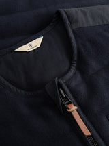Close-up of the BGdand Waistcoat in Dark Navy by Blue de Gênes, featuring quilted fabric with a smooth, subtly textured finish. The visible zipper is accented by a brown pull tab, while a cream-colored tag near the collar displays a small emblem and text.