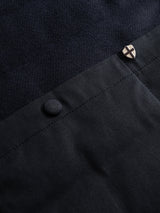 Close-up of the BGdand Waistcoat in dark navy by Blue de Gênes, showing its dark fabric with visible textures—one matte and one slightly textured—a button, and a small shield-shaped metallic pin featuring a cross design.