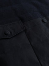 Close-up of the BGdand Waistcoat in Dark Navy by Blue de Gênes, highlighting a dark fabric with a flap pocket featuring two covered buttons on the left side. The detailed view clearly displays the fabric texture and precise stitching, evoking the craftsmanship of a classic utility or finely tailored quilted waistcoat.