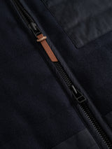 Close-up of a black zipper with a brown leather pull tab on dark fabric, featured on the BGdand Waistcoat in Dark Navy by Blue de Gênes.