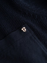 A small metal pin shaped like a shield with a cross design is attached to the pocket of the Blue de Gênes BGfraser Zip Knit in dark navy.