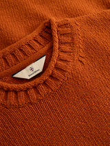 A close-up of the BGgordon Knit - Ginger Bread Orange wool sweater features a ribbed crew neck collar. A white label inside the collar displays the Blue de Gênes brand name with a small red and blue crest logo embroidered above it.