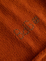 Close-up of the BGgordon Knit - Ginger Bread Orange sweater by Blue de Gênes, showing its orange wool knit fabric with “b4b” embroidered in dark brown thread as a striking detail on the surface.