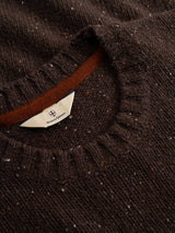 Close-up of the BGadamo Crewneck Knit in Hot Fudge Brown by Blue de Gênes, showcasing its dark brown speckled wool with multicoloured nep detailing throughout. The ribbed crew neckline is accented by a visible cream tag featuring the brand’s logo and text inside the collar.