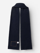 The BGcomforto Knit Scarf by Blue de Gênes is a long, ribbed wool scarf in dark navy, featuring a stitched rectangular patch and a small white tag at one end, shown against a plain white background.