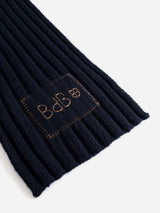 A close-up of the BGcomforto Knit Scarf in Dark Navy by Blue de Gênes, showcasing its ribbed wool texture and a rectangular patch adorned with embroidered symbols and letters in brown thread.