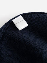A white clothing label reading 100% Lambswool is attached to the textured dark navy fabric of the BGboshi Beanie by Blue de Gênes, highlighting the cozy material of this ribbed turn-up wool accessory, shown against a plain white background.