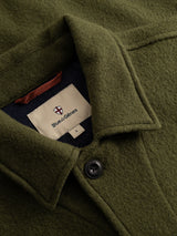 Close-up of the BGhew Wool Overshirt in Winter Moss, featuring an olive green boiled wool fabric with a visible button and an inner collar label displaying Blue de Gênes along with a small shield logo above the brand name.