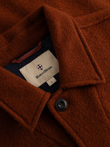 Close-up of the BGhew Wool Overshirt in Ginger Bread Orange boiled wool featuring a black button, with an interior fabric label displaying the Blue de Gênes shield logo and size L.