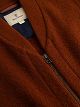 Close-up of the BGmudock Wool Waistcoat in Ginger Bread Orange, featuring a partially zipped front. A white label reading Blue de Gênes is sewn inside the collar, underscoring the rugged, workwear-inspired design of this piece.