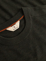 A close-up of the BGhamish Crewneck Knit in Beech Green, a dark, lightweight sweater by Blue de Gênes. The ribbed crewneck features a visible white label with a blue and red logo and branding inside the collar, accented by an orange inner seam detail. Expertly crafted from premium merino wool, this sweater seamlessly blends comfort and style in every stitch.