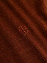 A close-up of the ginger bread orange, lightweight knit fabric of the Blue de Gênes BGhamish Crewneck Knit, featuring a small, embroidered shield-shaped design in slightly lighter thread at the center—perfect as a refined detail on this merino wool crewneck sweater.