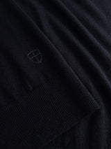 Close-up of the BGigor Polo Knit in Dark Navy by Blue de Gênes, highlighting the fine black knitted fabric and a small embroidered shield emblem for decoration near the ribbed cuff.