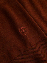 Close-up of the BGigor Polo Knit in Ginger Bread Orange by Blue de Gênes, featuring a brown, fine-gauge knit fabric with delicate ribbing at the edge and a small, stitched shield emblem adorned with a cross and dots at the center—perfect detailing for this refined merino wool polo.