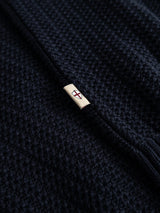 Close-up of the BGmurry Polo Knit in Dark Navy by Blue de Gênes, showcasing its textured knit fabric reminiscent of fine merino wool, and featuring a small cream tag with a red and blue stitched X inside a diamond.