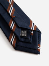 Close-up of the BGcarl Tie - Dark Navy by Blue de Gênes, featuring brown and white diagonal stripes on navy blue silk, folded neatly to reveal part of the tie label underneath.