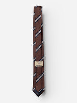 The BGcarl Tie - Ginger Bread Orange by Blue de Gênes is a brown silk tie featuring diagonal white, black, and blue stripes. Neatly folded with a beige label adorned with a blue and red crest and the Blue de Gênes name, this essential men’s accessory stands out against a plain white background.