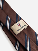 Elevate your style with the BGcarl Tie - Ginger Bread Orange by Blue de Gênes. This men’s accessory showcases striking brown stripes accented by blue and white diagonal lines, expertly crafted from premium silk. The tie is finished with a beige label featuring a red and white shield alongside the Blue de Gênes logo.