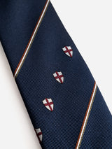 The BGshield Tie - Dark Navy by Blue de Gênes is a sophisticated silk necktie, featuring diagonal white and brown stripes accented with small shield emblems adorned with red crosses for an elegant touch.