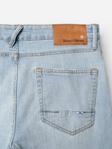 Close-up of the back waist and pocket of BGvinci Trueblue Jeans in mid blue denim by Blue de Gênes, featuring comfort stretch, a brown leather brand patch, and a small stitched flag detail on the pocket.