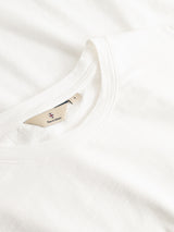A close-up of the neatly folded BGoscar T-Shirt - Snow Fall by Blue de Gênes, with a beige branded tag inside the crewneck, displayed on a white fabric background.