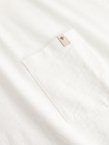 Close-up of the BGoscar T-Shirt - Snow Fall by Blue de Gênes, a white slub cotton tee with a chest pocket featuring a beige tag at the top and a small embroidered blue, red, and white emblem.