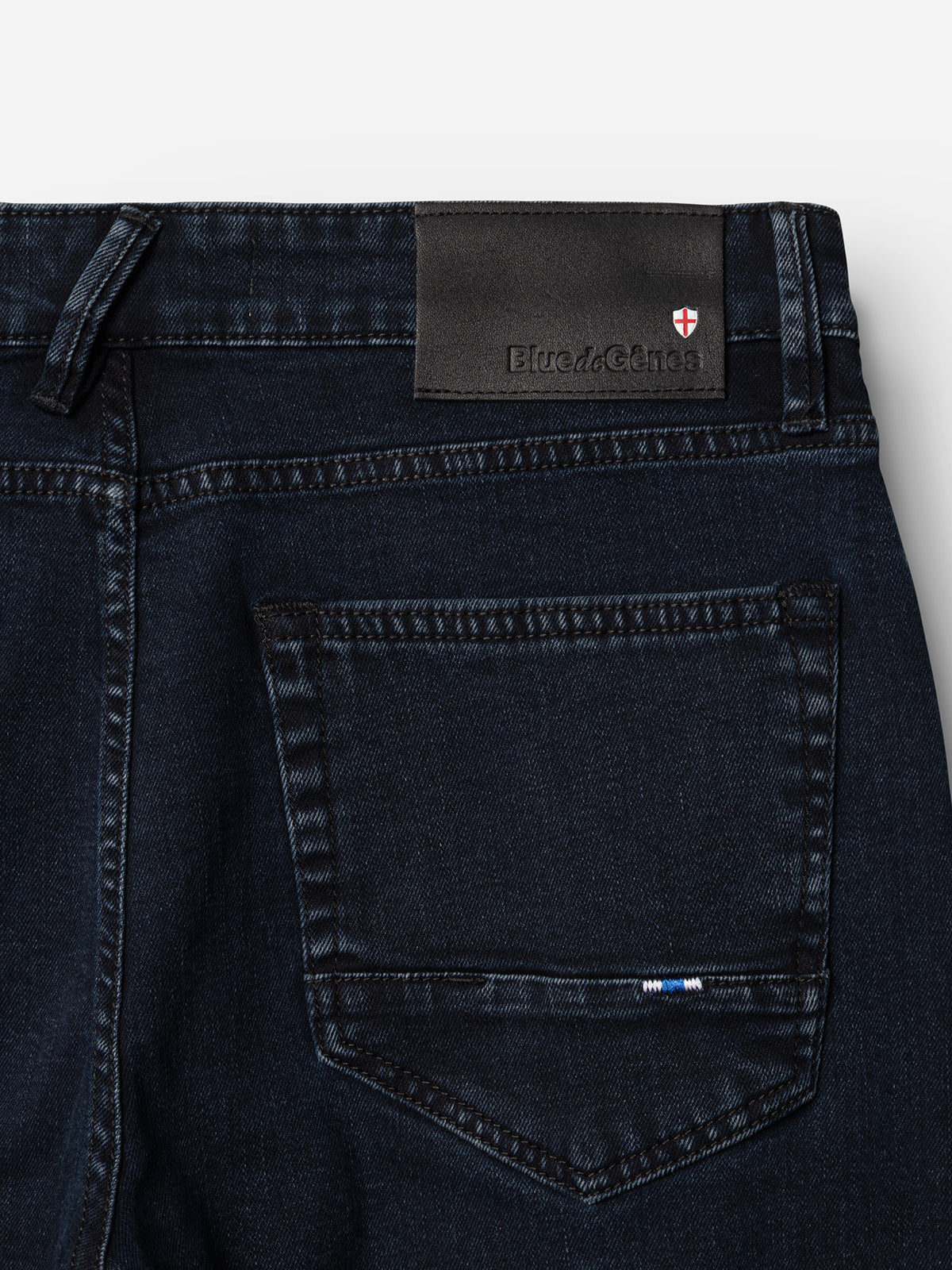 Close-up of the back pocket of Blue de Gênes BGvinci Black OD Jeans in blue black denim, featuring a black leather patch with text and a small red and white shield emblem above the pocket.