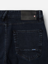 Close-up of the back pocket of Blue de Gênes BGvinci Black OD Jeans in blue black denim, featuring a black leather patch with text and a small red and white shield emblem above the pocket.