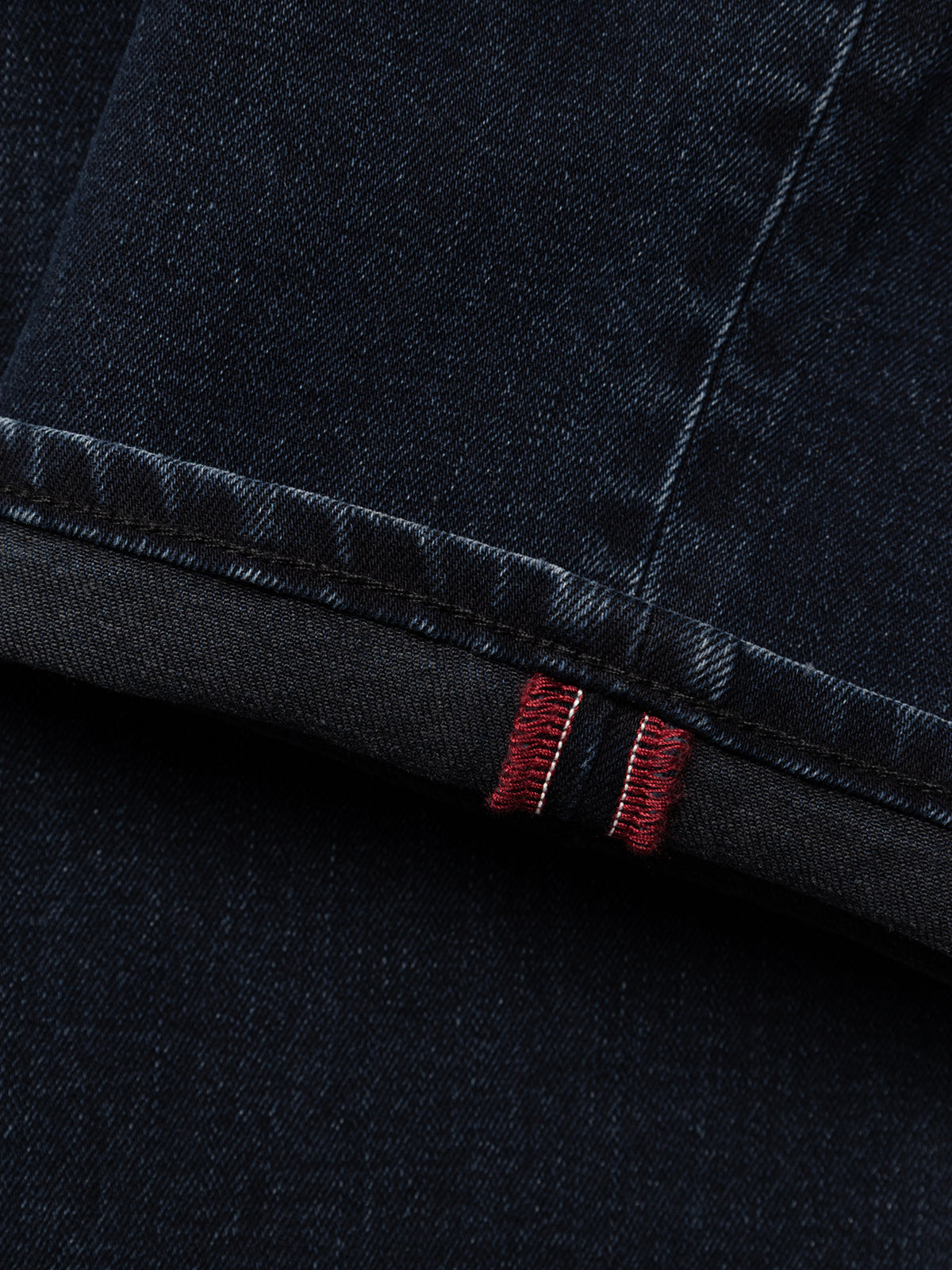 Close-up of the cuff of BGvinci Black OD Jeans by Blue de Gênes in blue black denim, showcasing a rolled hem with visible red and white selvedge stitching detail.