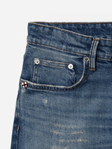 Close-up of the BGvinci Break Jeans - Denim wash by Blue de Gênes, showcasing a dark blue pocket with a small patch featuring a red cross on a white background, visible distressing on the comfort stretch denim fabric, and metal rivets near the seams.