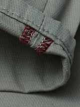 A close-up of the textured shadow green fabric from Blue de Gênes' BGpaulo Teo Pant showcases a rolled hem with two parallel lines of red stitching and white thread at the edge—details inspired by vintage military pants and the craftsmanship characteristic of durable chinos.