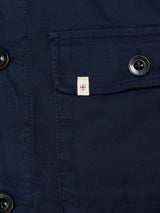 Close-up of the BGpontus Teo Overshirt in Dark Navy by Blue de Gênes, featuring textured cotton fabric, black buttons, and a flap pocket. A small white tag with a red cross emblem is sewn beneath the pocket flap, accentuating the piece’s relaxed fit.